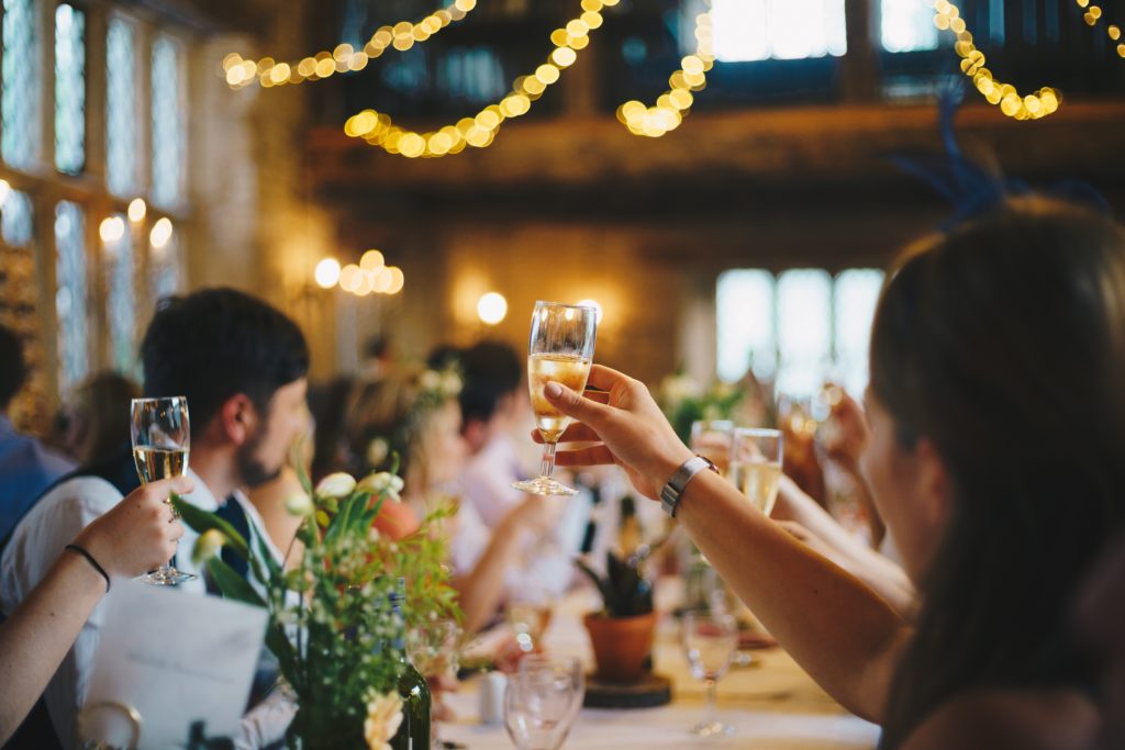 Wedding-guests-sitting-at a-table-raising-champagne-glasses-under-string-lights