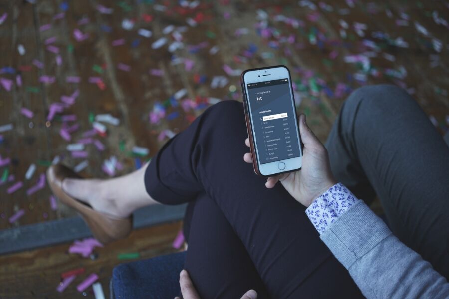 Person holding iPhone displaying Competitions leaderboard, with confetti on the floor